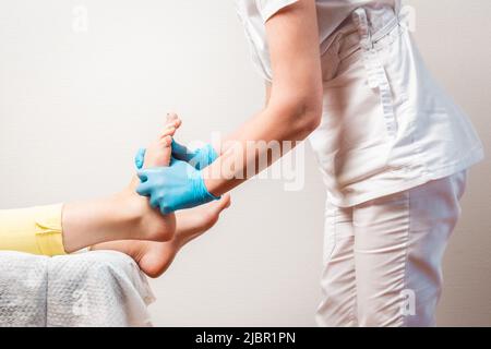 Ein Podologe massiert die Füße des Kunden. Nahaufnahme der Beine und der Hände des Meisters. Speicherplatz kopieren. Das Konzept der Pediküre und Chiropody. Stockfoto