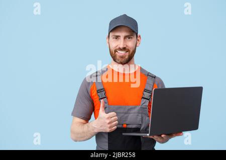 Schöner lächelnder Mann in Uniform mit Laptop, der auf blauem Hintergrund die Kamera anschaut Stockfoto