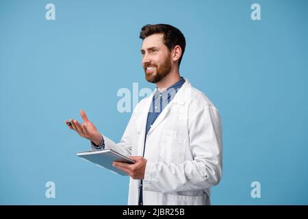 Der Arzt konsultiert den Patienten, der die Tablette in den Händen hält, die über dem blauen Hintergrund des Studios stehen Stockfoto