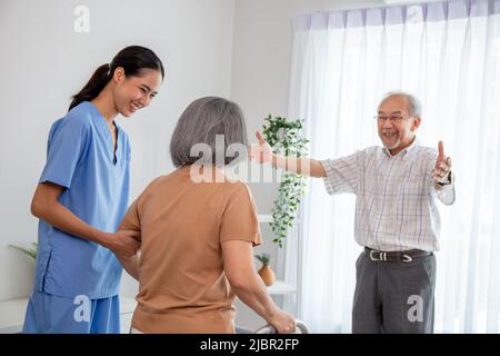 Asiatische junge Krankenschwester kümmern ein Senior mit einem Wanderer. Eine Krankenschwester mit einem Patienten versucht, in einem pensionierten Hausdienst zu gehen. Stockfoto