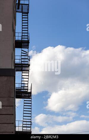 Silhouette einer Feuerflucht auf einem Hochhaus vor einem blauen Himmel mit Wolken. Einige der Treppen sind kaputt. Es ist freier Speicherplatz für Text vorhanden Stockfoto