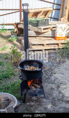 Kochen von Speisen oder Pilaf in einem Kessel auf Feuer. Kochen im Kessel auf offenem Feuer in der Natur. Bowler auf Lagerfeuer im Wald. Feuerflamme in Nahaufnahme. Speicherplatz kopieren. Stockfoto