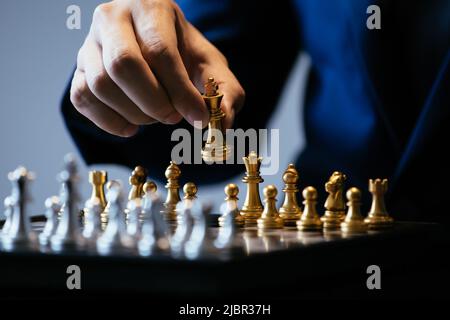 Nicht erkennbare Mann in Anzug und goldene König beim Schach spielen gegen grauer Hintergrund Stockfoto