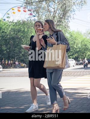 25. Mai, Russland, Tomsk, zwei Mädchen gehen im Sommer auf der Straße und essen einen Kuchen Editorial Stockfoto