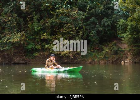 Ein frustrierter, gelangweilter bärtiger Mann sitzt in einem Kajak. Speicherplatz kopieren. Das Konzept eines Problems auf einer Wasserreise. Stockfoto