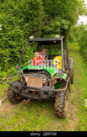 Junge, der in einem John Deere Gator Utility Vehicle, High Bickington, Devon, England, Vereinigtes Königreich, fährt. Stockfoto