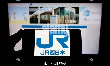 Person, die das Smartphone mit dem Logo der japanischen Firma West Japan Railway (JR) auf dem Bildschirm vor der Website hält. Konzentrieren Sie sich auf die Telefonanzeige. Stockfoto