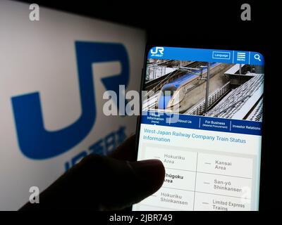 Person, die das Smartphone mit der Webseite der japanischen Firma West Japan Railway (JR) auf dem Bildschirm vor dem Logo hält. Konzentrieren Sie sich auf die Mitte des Telefondisplays. Stockfoto