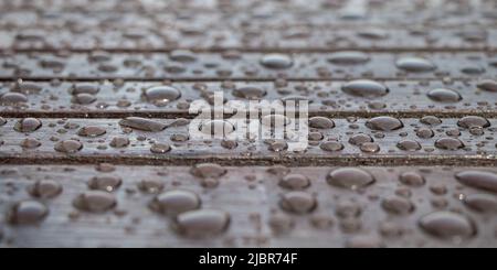 Holzplanken mit Wassertropfen bedeckt, Hintergrund für regnerisches Wetter. Nasse braune Bretter aus der Nähe. Selektiver Fokus Stockfoto