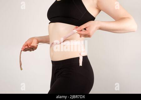 Eine Frau misst den Umfang des Abdomens mit einem Zentimeter großen Klebeband, Nahaufnahme. Schlankheitskonzept Stockfoto