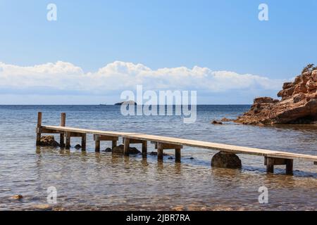 Мan-made hölzerne schmale Pier auf Cala Bonita, am Horizont eine kleine Insel. Ibiza, Balearen, Spanien Stockfoto