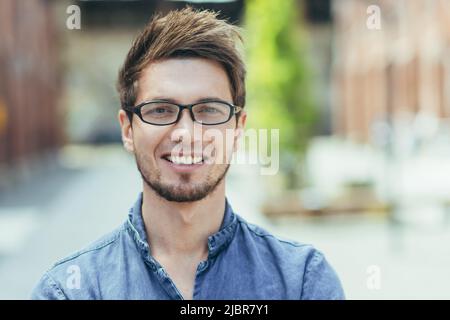 Nahaufnahme eines jungen Mannes mit Bart, eines freiberuflichen Geschäftsmannes in einer Brille, der lächelnd auf die Kamera blickt Stockfoto