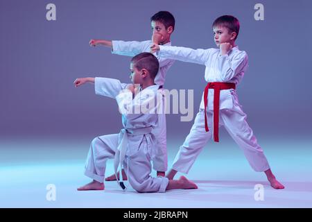 Gruppe von Kindern, verschiedenen Jungen, Taekwondo Athleten in weißen doboks in Aktion isoliert auf lila Farbe Hintergrund. Konzept des Sports, Kampfkunst Stockfoto