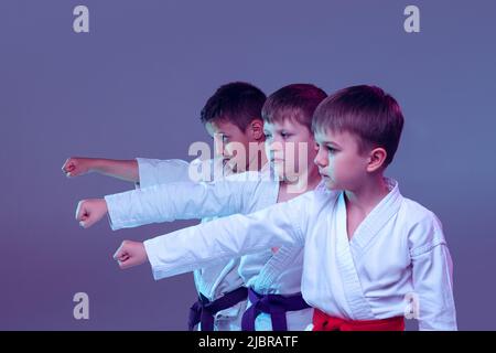 Gruppe von Kindern, verschiedenen Jungen, Taekwondo Athleten in weißen doboks in Aktion isoliert auf lila Farbe Hintergrund. Konzept des Sports, Kampfkunst Stockfoto