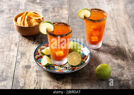 Hausgemachter Michelada-Cocktail mit Bier, Limettensaft, heißer Sauce, gesalzenem Rand und Tomatensaft auf dem Holztisch Stockfoto