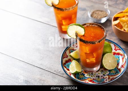 Hausgemachter Michelada-Cocktail mit Bier, Limettensaft, heißer Sauce, gesalzenem Rand und Tomatensaft auf dem Holztisch Stockfoto