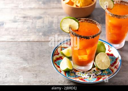 Hausgemachter Michelada-Cocktail mit Bier, Limettensaft, heißer Sauce, gesalzenem Rand und Tomatensaft auf dem Holztisch Stockfoto