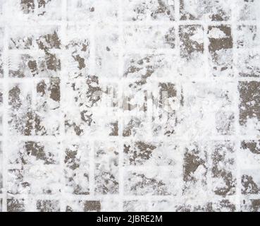 Verschneite Straßenkacheln. Steinmauerwerk auf dem Bürgersteig. Fußabdruck im Schnee von einem Stiefel aus Stockfoto