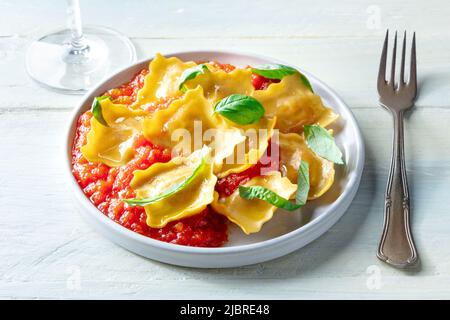 Ravioli mit Tomatensauce und frischen Basilikumblättern auf einem Teller, italienisches Abendessen, auf einem Holztisch mit einem Glas Wein Stockfoto