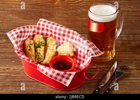 Fischfilet im Teig mit Kräutern, Sauce und tschechischem Bier auf Holztisch Stockfoto