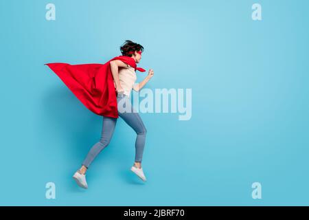 In voller Länge Foto von ziemlich starken Frau tragen roten Umhang springen hoch weglaufen leeren Raum isoliert blauen Hintergrund Stockfoto