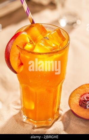 Sommerliche kalte Getränke: Pfirsich-Sangria mit Eiswürfeln im Glas auf Sandboden Stockfoto