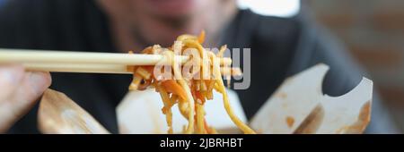 Lächelnder Mann, der würzige Nudel isst chinesisches Essen mit Gemüse mit Essstäbchen Stockfoto
