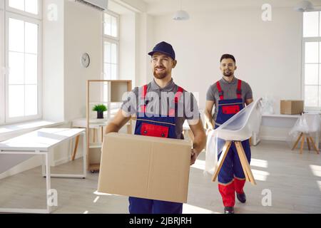 Zwei glückliche junge Arbeiter vom LKW-Lieferservice, die Möbel und Kisten trugen Stockfoto
