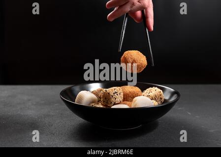 Die Hand eines Mannes mit Essstäbchen nimmt ein asiatisches Dessert-Mochi. Japanische Küche. Stockfoto