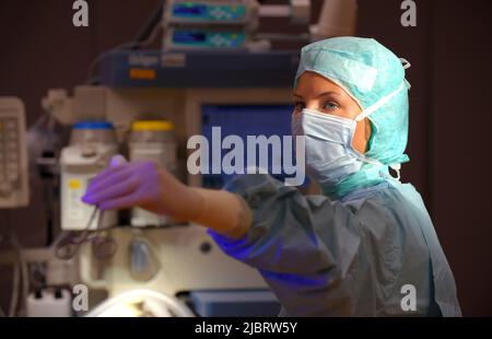 Eine Frau wird in einem Operationssaal des Krankenhauses gesehen. Sie ist vollständig als eine Anstationsschwester mit einer Gesichtsmaske und steriler medizinischer OP-Kleidung gekleidet. Stockfoto