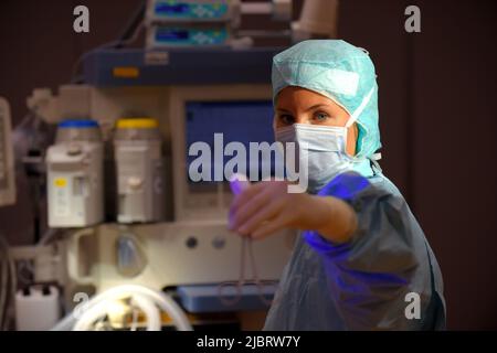 Eine Frau wird in einem Operationssaal des Krankenhauses gesehen. Sie ist vollständig als eine Anstationsschwester mit einer Gesichtsmaske und steriler medizinischer OP-Kleidung gekleidet. Stockfoto