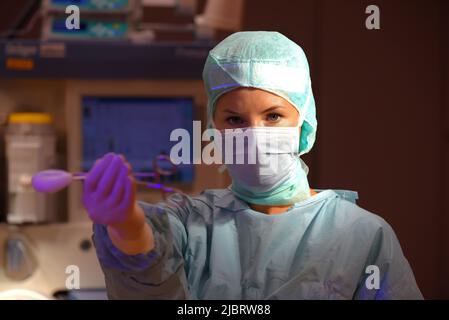 Eine Frau wird in einem Operationssaal des Krankenhauses gesehen. Sie ist vollständig als eine Anstationsschwester mit einer Gesichtsmaske und steriler medizinischer OP-Kleidung gekleidet. Stockfoto