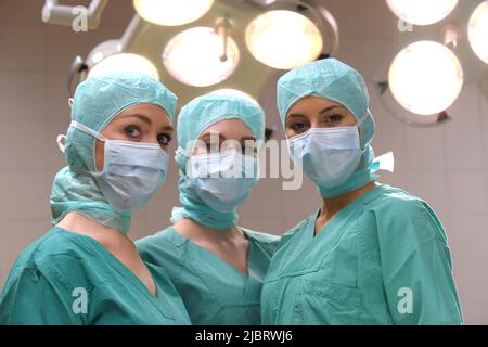 Drei Krankenschwestern werden in einem Operationssaal gesehen. Sie sind als OP-Krankenschwestern mit Gesichtsmasken und steriler OP-Kleidung gekleidet Stockfoto