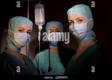 Drei Krankenschwestern werden in einem Operationssaal gesehen. Sie sind als OP-Krankenschwestern mit Gesichtsmasken und steriler OP-Kleidung gekleidet Stockfoto