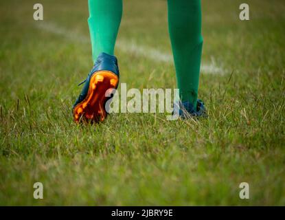 Fußballspieler in Fußballschuhen beim Gehen auf Gras mit selektivem Fokus. Stockfoto