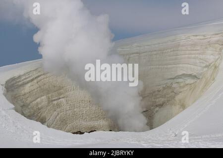Dampf steigt aus einer Vulkanfumarole, die von Schnee umgeben ist Stockfoto