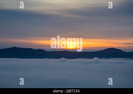 Bei Sonnenaufgang fielen neblige Wolken unter die Höhe des Berges, oranger Horizont Stockfoto