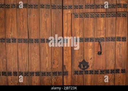 Doppeltür aus massivem lackiertem und gealtertem Holz mit antiken Metalldekorationen, Klopfer und Schloss in Schwarz Stockfoto