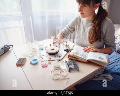 Lifestyle-Konzept, arbeiten von zu Hause aus, um Ihr Leben neu zu erfinden - Schmuck Designer Arbeitsplatz. Frau macht Schmuck. Georgianische Herstellung von Minankari-Emaille. Juwelier macht Zubehör in der Werkstatt. Stockfoto