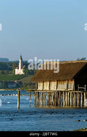 Deutschland, Baden-Württemberg, Bodensee, Uhldingen-Mühlhofen, Unteruhldingen, Pfahlbaumuseum, Pfahlbautenwohnung, Pfahlbauten, von der UNESCO zum Weltkulturerbe erklärt, und im Hintergrund die Wallfahrtskirche Birnew Stockfoto