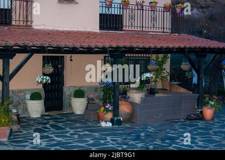 Dekorativer hängender Blumentopf mit Korbtopf aus blauen Blumen auf der Veranda mit Schieferboden Stockfoto