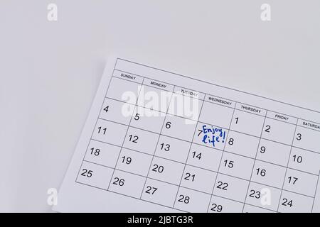 Genießen Sie das Leben handwriting auf dem Papierkalender auf weißem Hintergrund. Draufsicht flach liegend. Stockfoto