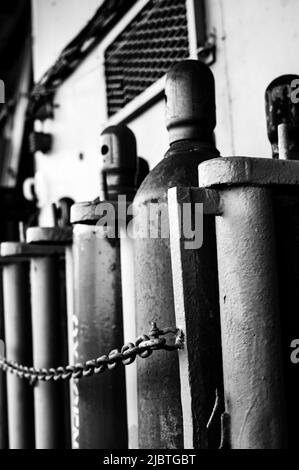 Druckgasflaschen, die vertikal durch eine Metallkette gesichert gelagert werden. Stockfoto