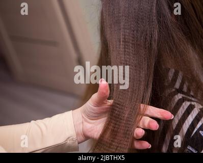 Nahaufnahme der Hand einer Frau, die einen welligen Haarsträhnen hält. Der Friseur macht eine Frisur für eine junge Frau. Friseur, Geschäftskonzept. Schönheitssalon, Haarpflege. Stockfoto