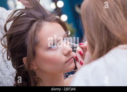 Ein professioneller Make-up-Künstler malt das Auge eines Kunden mit einem Pinsel. Weibliche Meisterin macht einer jungen Frau Make-up. Geschäftskonzept - Schönheitssalon, Gesichtshautpflege, Kosmetik. Stockfoto