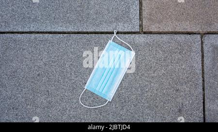 Karlsruhe, Deutschland - 28. Aug 2021: Blaue medizinische Maske auf Kopfsteinpflaster. Draufsicht. Stockfoto