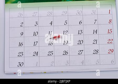 Rote Stecknadel auf einem weißen Monatskalender. Markieren eines Tages für einen Termin oder eine Veranstaltung. Stockfoto