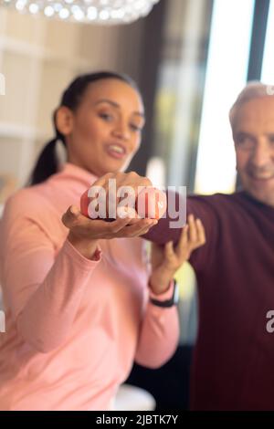 Biraziale Physiotherapeutin, die kaukasischen älteren Mann bei der Dehnung der Hand mit Hantel unterstützt Stockfoto