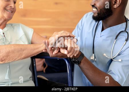 afroamerikanischer Gesundheitshelfer unterstützt kaukasische ältere Frau, die auf dem Rollstuhl sitzt Stockfoto