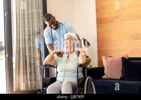afroamerikanischer Gesundheitshelfer unterstützt kaukasische ältere Frau, die auf dem Rollstuhl sitzt Stockfoto